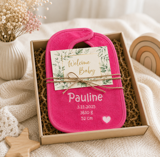 Pinkes Lätzchen mit Pauline und Geburtsdaten, als Geschenk mit Welcome-Baby-Karte in einer Box arrangiert