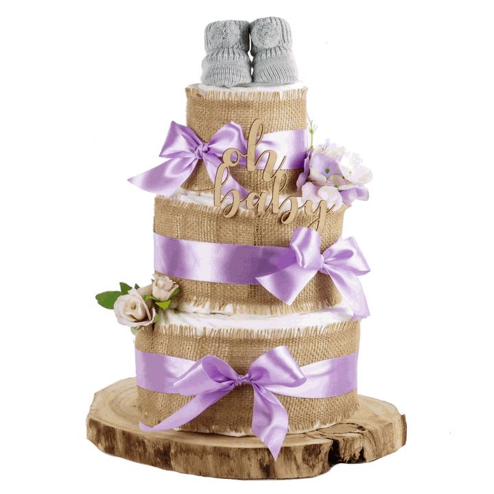 Dreistöckige Windeltorte mit Jute, fliederfarbenen Schleifen, Blumen und grauen Babyschuhen auf einer Holzscheibe